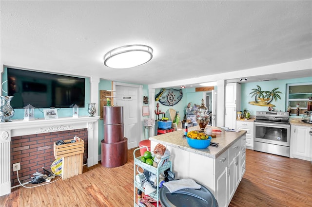 kitchen with stainless steel electric stove, white cabinets, a kitchen island, a textured ceiling, and light hardwood / wood-style flooring