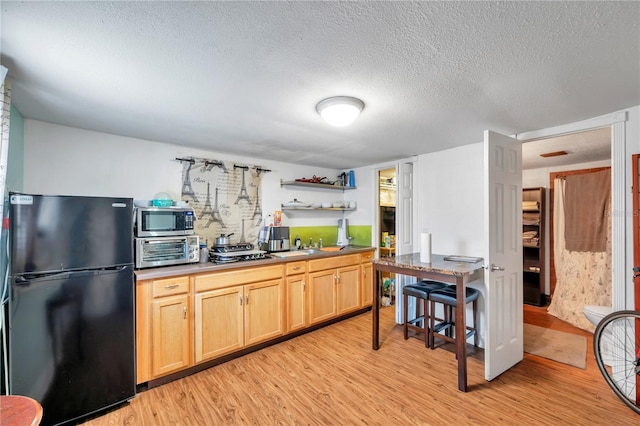 kitchen with light brown cabinetry, a textured ceiling, light hardwood / wood-style floors, and black refrigerator