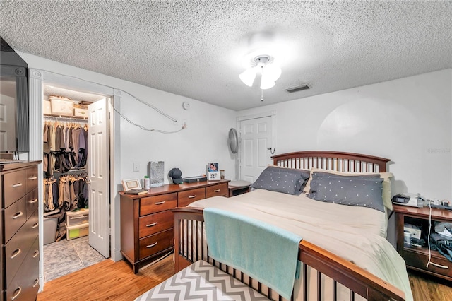 bedroom featuring light wood-type flooring, a textured ceiling, a spacious closet, and a closet