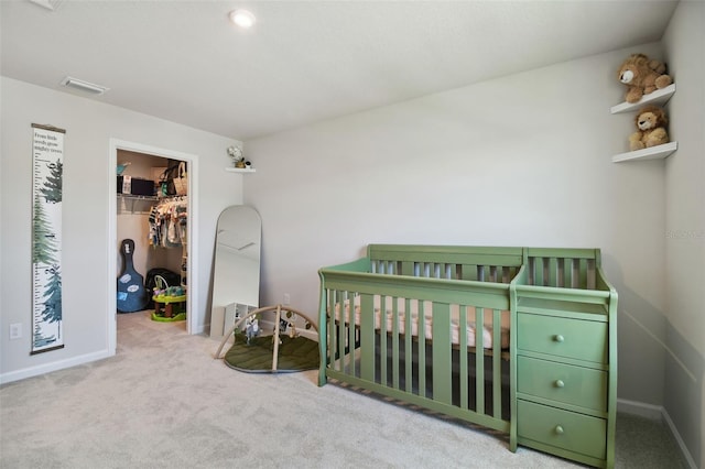 bedroom featuring a crib, light carpet, a walk in closet, and a closet