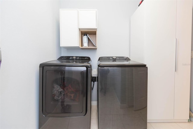 washroom with washing machine and clothes dryer, light tile patterned floors, and cabinets