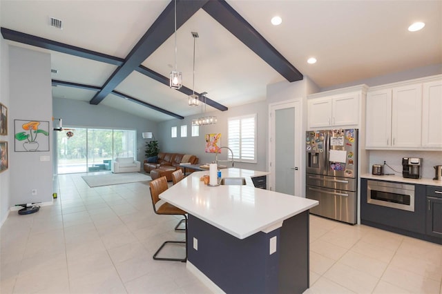 kitchen with white cabinetry, vaulted ceiling with beams, pendant lighting, a kitchen island with sink, and appliances with stainless steel finishes