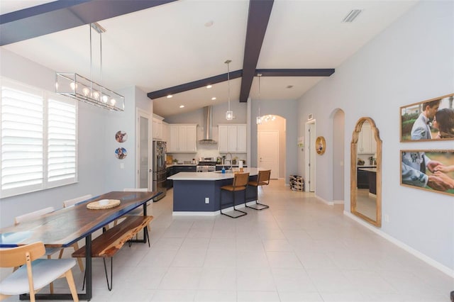 kitchen featuring a kitchen island with sink, hanging light fixtures, beamed ceiling, white cabinets, and wall chimney range hood