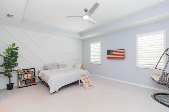 carpeted bedroom with ceiling fan and a tray ceiling