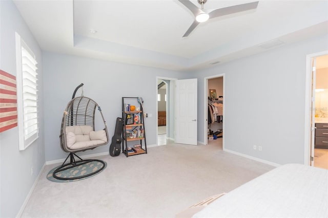 bedroom featuring a raised ceiling, light carpet, ceiling fan, a walk in closet, and ensuite bath