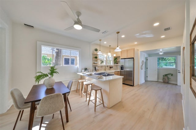 kitchen featuring hanging light fixtures, a wealth of natural light, a kitchen breakfast bar, and stainless steel fridge