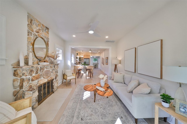 living room featuring a stone fireplace, light wood-type flooring, and ceiling fan