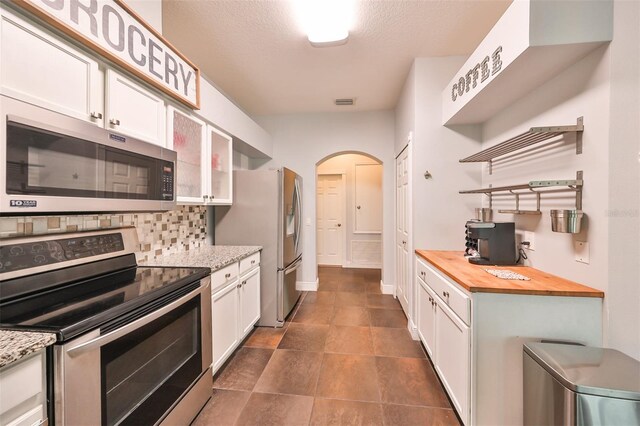 kitchen featuring a textured ceiling, white cabinetry, appliances with stainless steel finishes, decorative backsplash, and butcher block counters