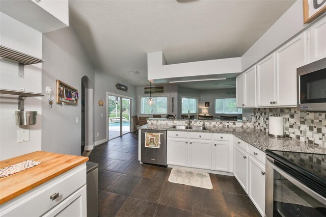 kitchen with tasteful backsplash, sink, white cabinetry, kitchen peninsula, and appliances with stainless steel finishes