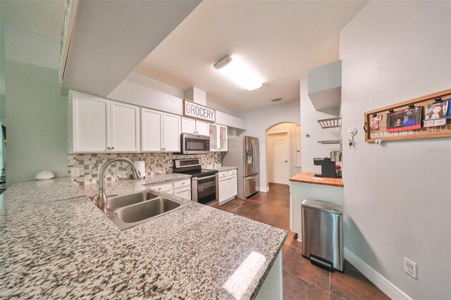 kitchen with white cabinets, sink, stainless steel appliances, light stone countertops, and decorative backsplash