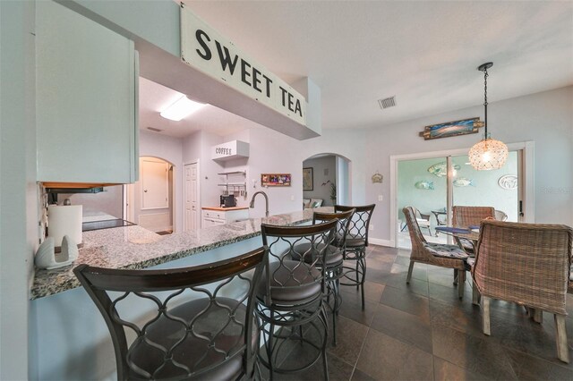 kitchen with light stone counters, sink, kitchen peninsula, decorative light fixtures, and an inviting chandelier