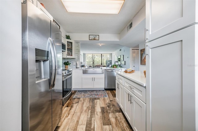 kitchen with white cabinetry, kitchen peninsula, stainless steel appliances, a textured ceiling, and wood-type flooring