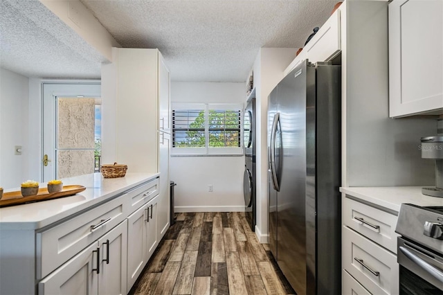 kitchen featuring stacked washing maching and dryer, dark wood-type flooring, stainless steel appliances, and white cabinets