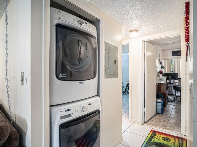 laundry area with light tile patterned floors, electric panel, a textured ceiling, and stacked washer / dryer