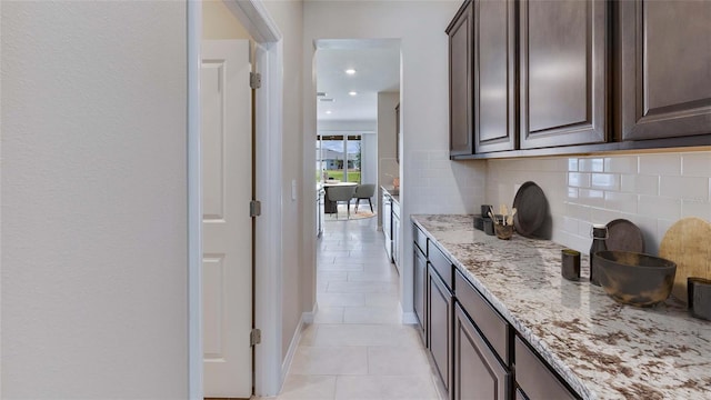 kitchen featuring dark brown cabinets, light stone counters, light tile patterned flooring, and backsplash