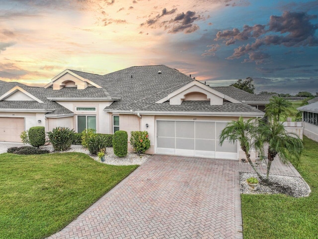 view of front of house with decorative driveway, stucco siding, a shingled roof, a garage, and a front lawn