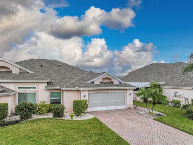 view of front of house featuring a garage, roof with shingles, decorative driveway, a front lawn, and stucco siding