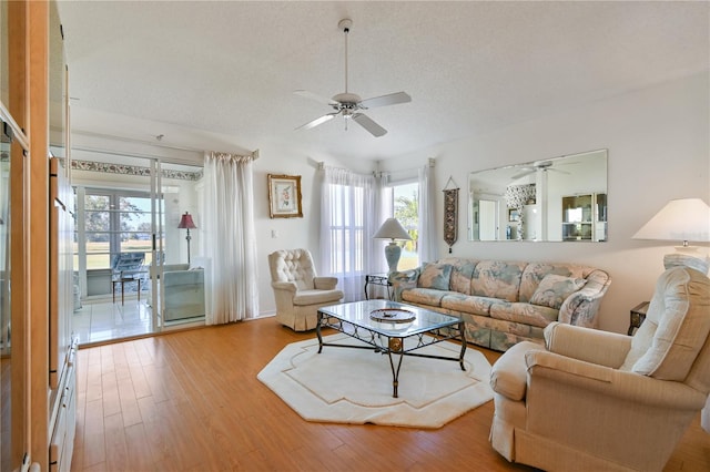 living room featuring ceiling fan, light wood-type flooring, and a textured ceiling