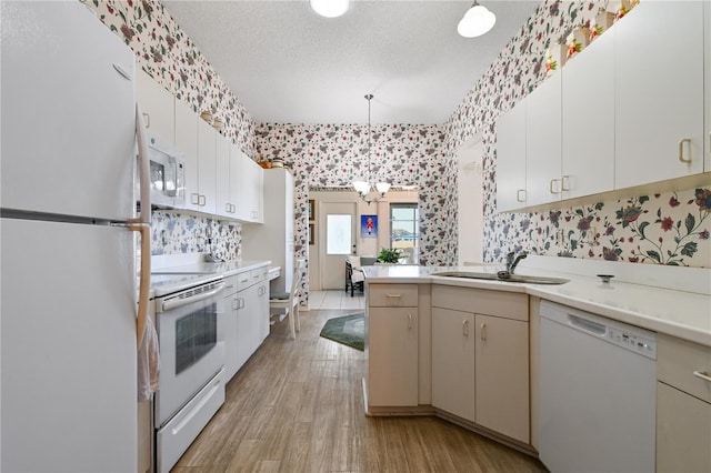 kitchen featuring white appliances, sink, decorative light fixtures, light hardwood / wood-style flooring, and an inviting chandelier