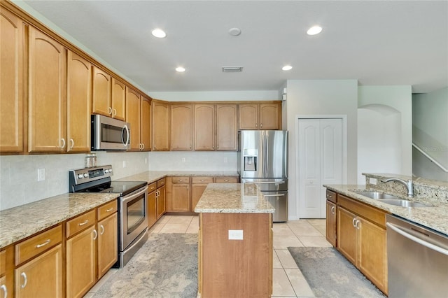 kitchen featuring appliances with stainless steel finishes, a kitchen island, sink, and light stone counters