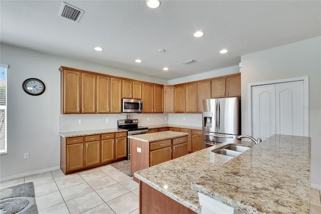 kitchen with sink, light tile patterned floors, a center island with sink, stainless steel appliances, and light stone countertops