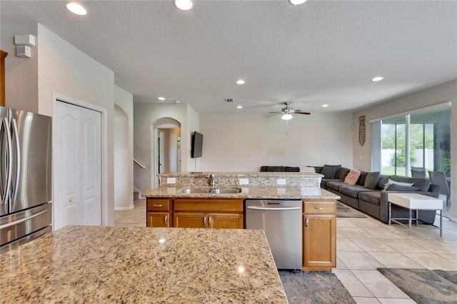 kitchen with a textured ceiling, sink, appliances with stainless steel finishes, light stone countertops, and ceiling fan