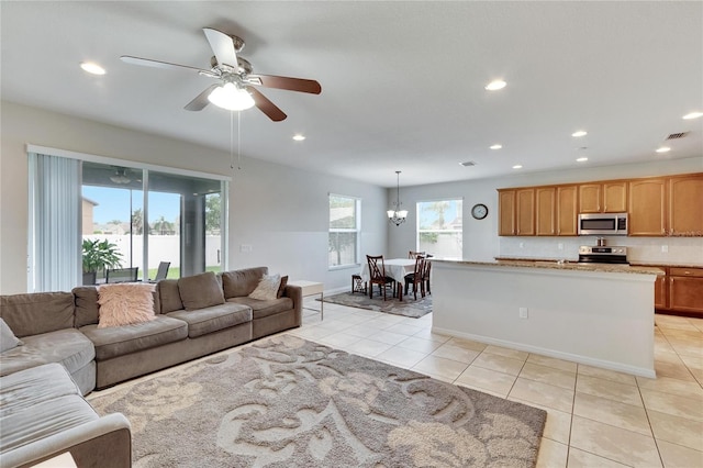 tiled living room featuring ceiling fan with notable chandelier and a wealth of natural light