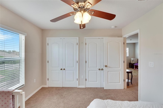 bedroom with multiple closets, ceiling fan, and light colored carpet