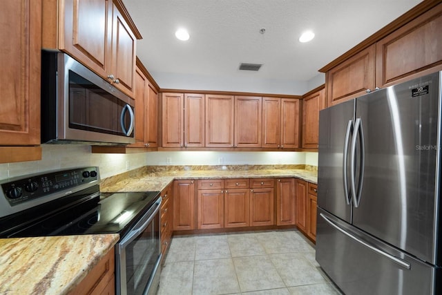 1030 Bellasol Way Unit 201, Apollo Beach, FL 33572 - kitchen featuring appliances with stainless steel finishes, brown cabinets, light tile patterned floors, light stone countertops, and recessed lighting