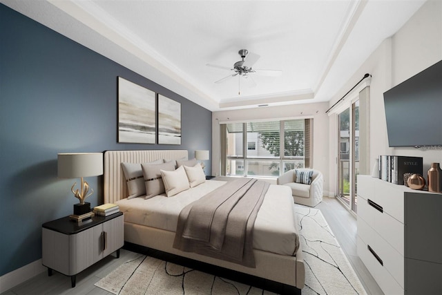 bedroom with light hardwood / wood-style flooring, a tray ceiling, and ceiling fan