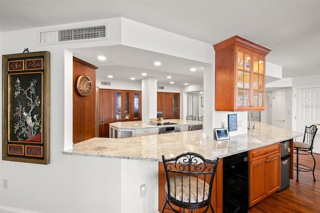 kitchen featuring a kitchen breakfast bar, kitchen peninsula, dark hardwood / wood-style floors, and light stone counters