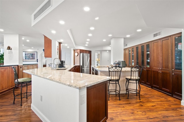 kitchen featuring light stone countertops, stainless steel fridge, a kitchen bar, and dark hardwood / wood-style floors