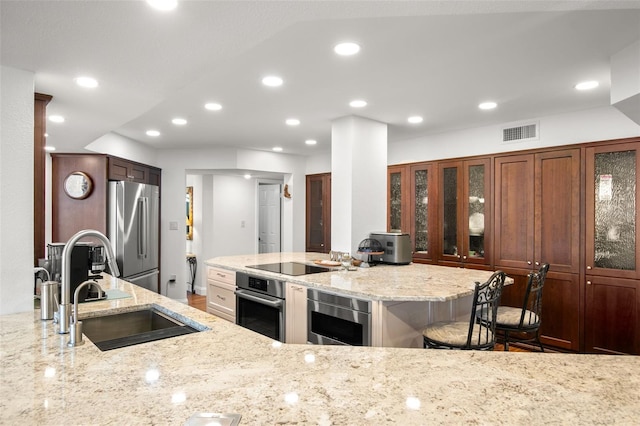 kitchen with light stone countertops, stainless steel appliances, a kitchen breakfast bar, and sink