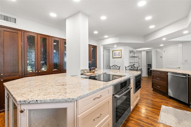 kitchen with light stone counters, stainless steel appliances, dark wood-type flooring, and a center island