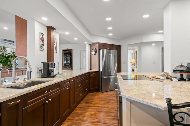 kitchen with stainless steel refrigerator, black electric stovetop, sink, and light stone counters