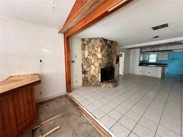 unfurnished living room featuring a textured ceiling, light tile patterned floors, and a stone fireplace