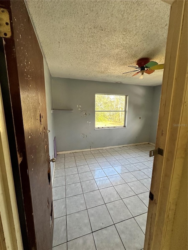 spare room featuring ceiling fan, light tile patterned floors, and a textured ceiling