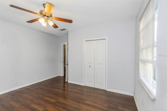 unfurnished bedroom with a textured ceiling, ceiling fan, dark wood-type flooring, and a closet