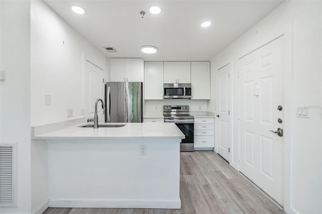 kitchen featuring appliances with stainless steel finishes, light wood-type flooring, kitchen peninsula, and white cabinetry