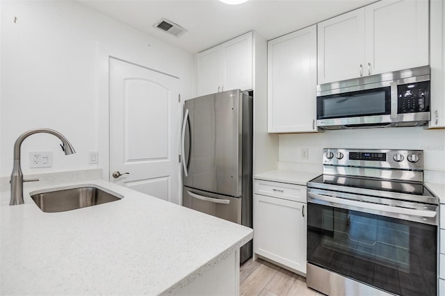 kitchen with appliances with stainless steel finishes, light hardwood / wood-style floors, white cabinetry, and sink