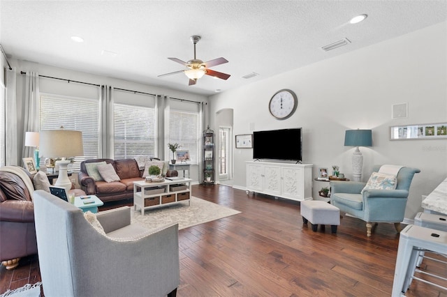 living room with a textured ceiling, ceiling fan, and dark wood-type flooring