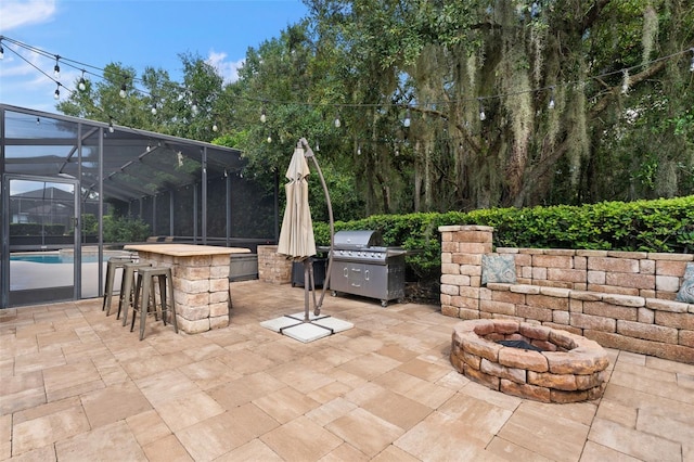 view of patio featuring area for grilling, a fire pit, exterior bar, and glass enclosure