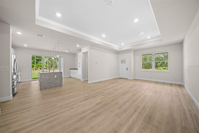 unfurnished living room with light hardwood / wood-style flooring, a tray ceiling, and ornamental molding