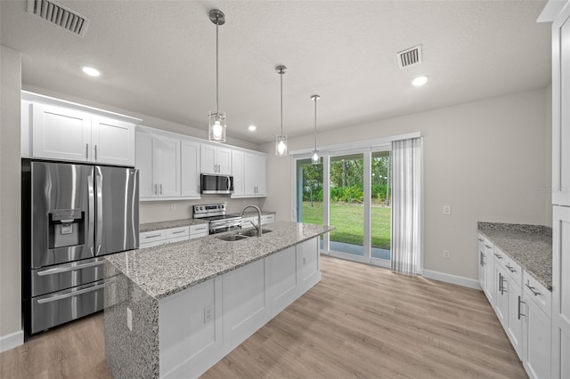 kitchen with appliances with stainless steel finishes, hanging light fixtures, white cabinets, light hardwood / wood-style flooring, and sink