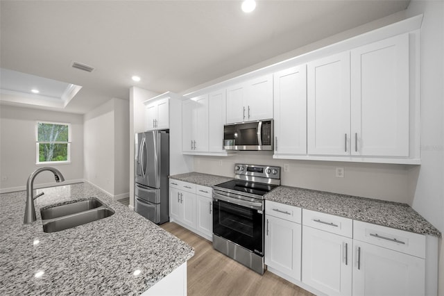 kitchen with white cabinets, stainless steel appliances, sink, and light stone countertops