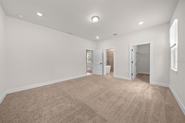 unfurnished bedroom with multiple windows, a closet, light colored carpet, ensuite bathroom, and a spacious closet