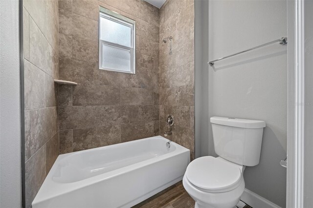 bathroom featuring wood-type flooring, tiled shower / bath combo, and toilet