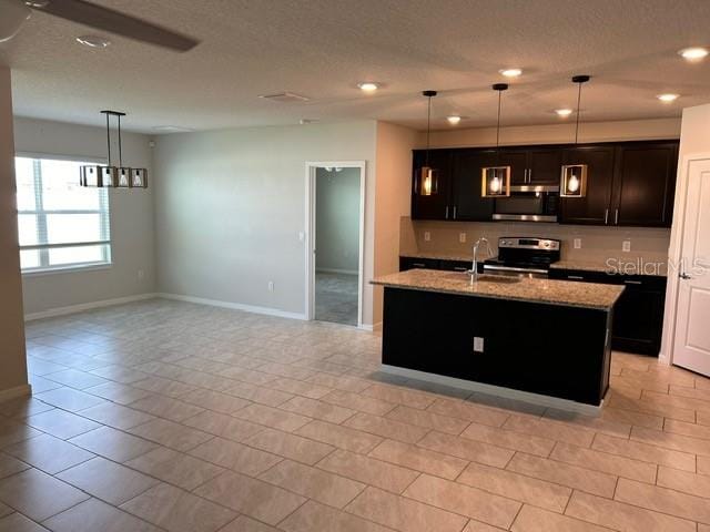 kitchen featuring pendant lighting, a kitchen island with sink, sink, appliances with stainless steel finishes, and light stone countertops