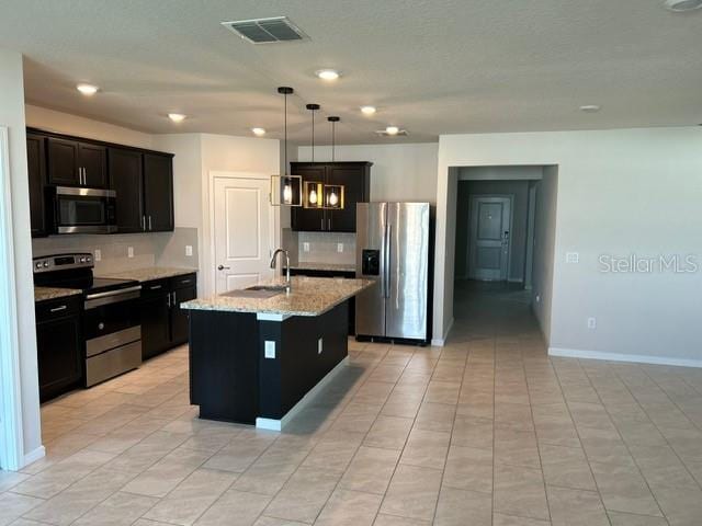 kitchen featuring an island with sink, sink, decorative light fixtures, appliances with stainless steel finishes, and light stone countertops