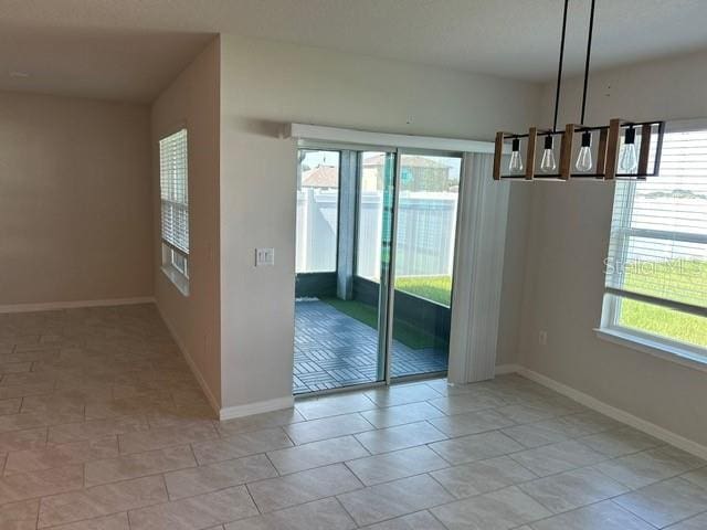 unfurnished dining area with a chandelier, healthy amount of natural light, and baseboards